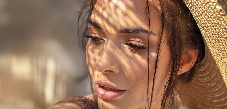 Portrait of beautiful young woman wearing summer hat . Closeup face of attractive girl posing in sunny vacation day.